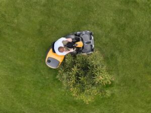 mand demonstrerer knækstyring på en stiga frontklipper ved at klippe rundt om en busk